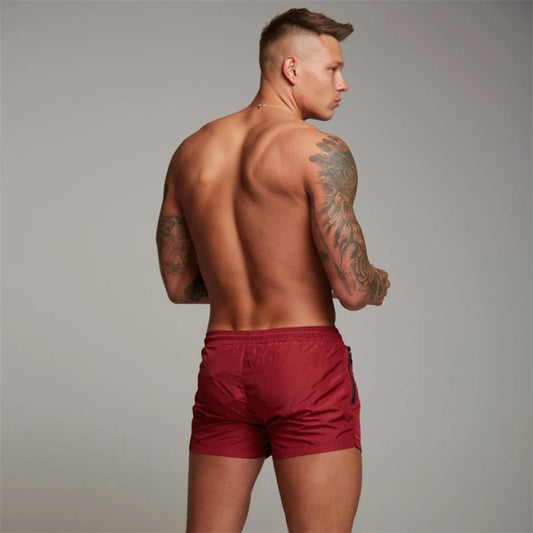 Mann in roten Badehosen, muskulös, tätowiert, Rückenansicht, Sportmode, Herrenbekleidung.