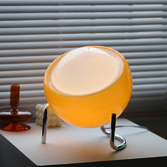 Gelbe Tischlampe aus Glas, modernes Design, auf weißem Tisch vor Jalousien.