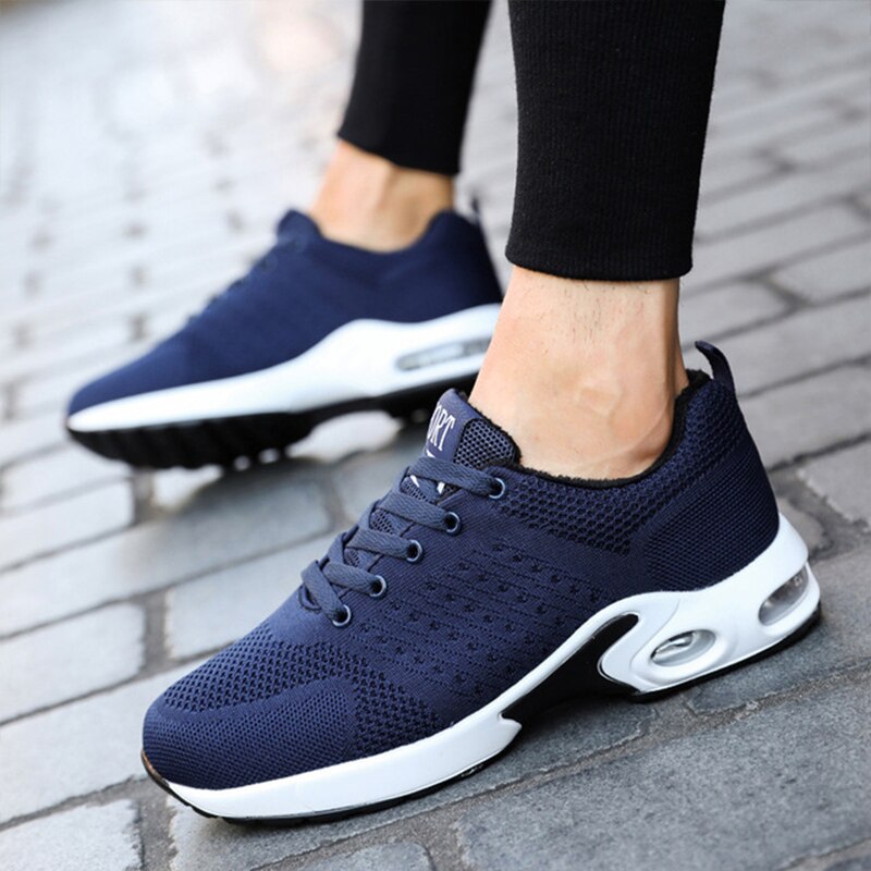 Dunkelblaue Herren-Sneaker, atmungsaktiv, sportlich, mit weißer Sohle auf Gehweg.