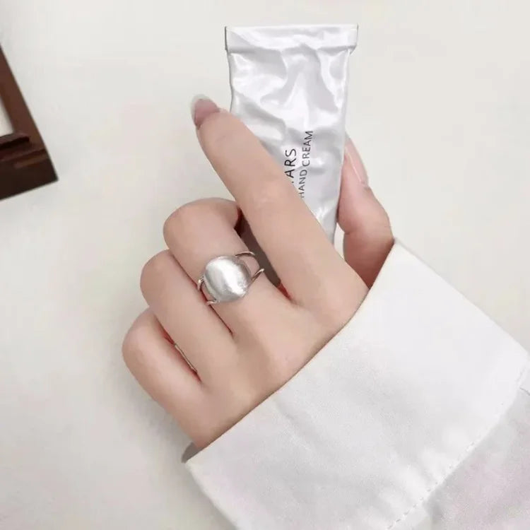 Silberner Ring an Hand mit weißer Bluse, hält Handcreme-Tube, elegantes Schmuckdesign.