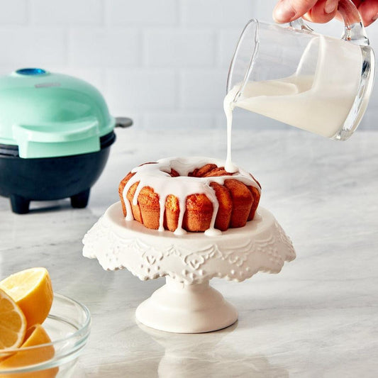 Elektrische Kuchenmaschine, türkis, mit kleinem Gugelhupf auf weißer Tortenplatte, Zuckerguss.
