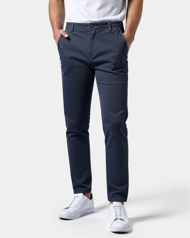 Mörkblå chinos framifrån på en modell med vit t-shirt och vita sneakers, båda händerna i fickorna. 15