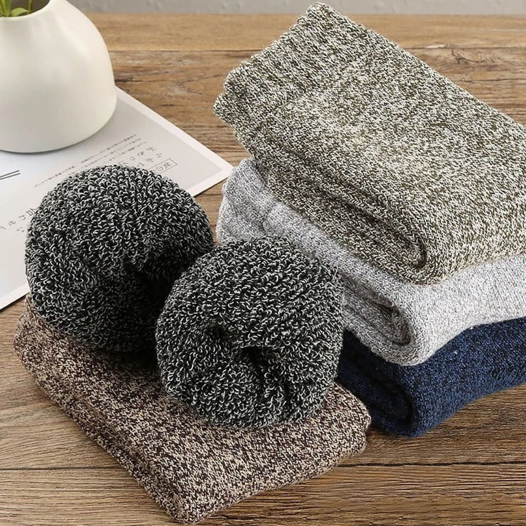 Mehrfarbige Stricksocken aus Wolle, gestapelt auf Holztisch, gemütliche Winterkleidung.