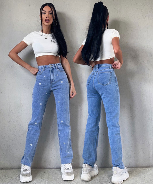 Frau in blauer Jeans mit Herzmuster, weißem Crop-Top, weißen Sneakern, modisch, lässig.