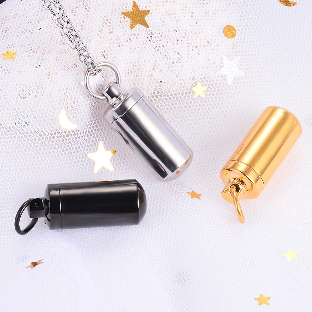 Drei zylindrische Urnen-Anhänger aus Edelstahl in Gold, Schwarz und Silber auf weißem Hintergrund.