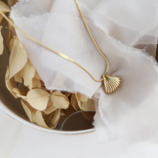 Goldene Muschelkette auf weißem Stoff, elegantes Schmuckdesign, Damenaccessoire.