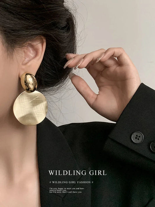 Frau mit großen, goldenen Ohrringen und schwarzem Blazer, elegante Modeaccessoires.