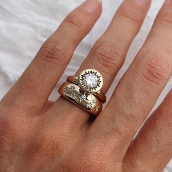 Damenhand mit drei goldenen Ringen, einer mit großem Diamant, auf weißem Hintergrund.