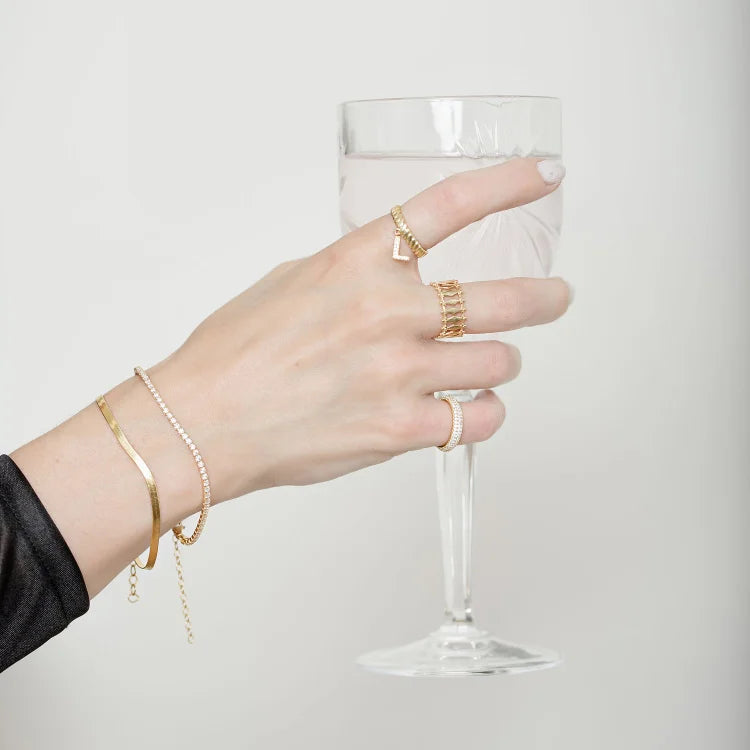 Hand mit goldenen Ringen und Armbändern hält ein Weinglas, eleganter Schmuck, minimalistisch.