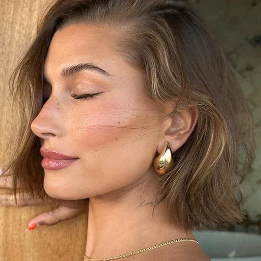 Frau mit kurzen braunen Haaren, goldene Ohrringe, geschlossene Augen, natürlicher Look.