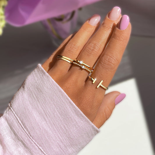 Frau mit rosa Maniküre trägt goldene Ringe, darunter ein Diamantring, auf der linken Hand.