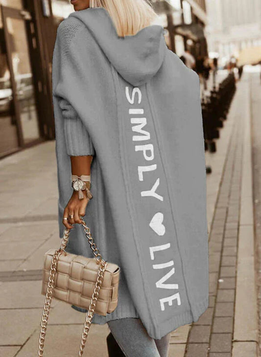 Frau in grauem Kapuzenmantel mit "Simply Live"-Aufdruck, beige Tasche, Stadtstraße.