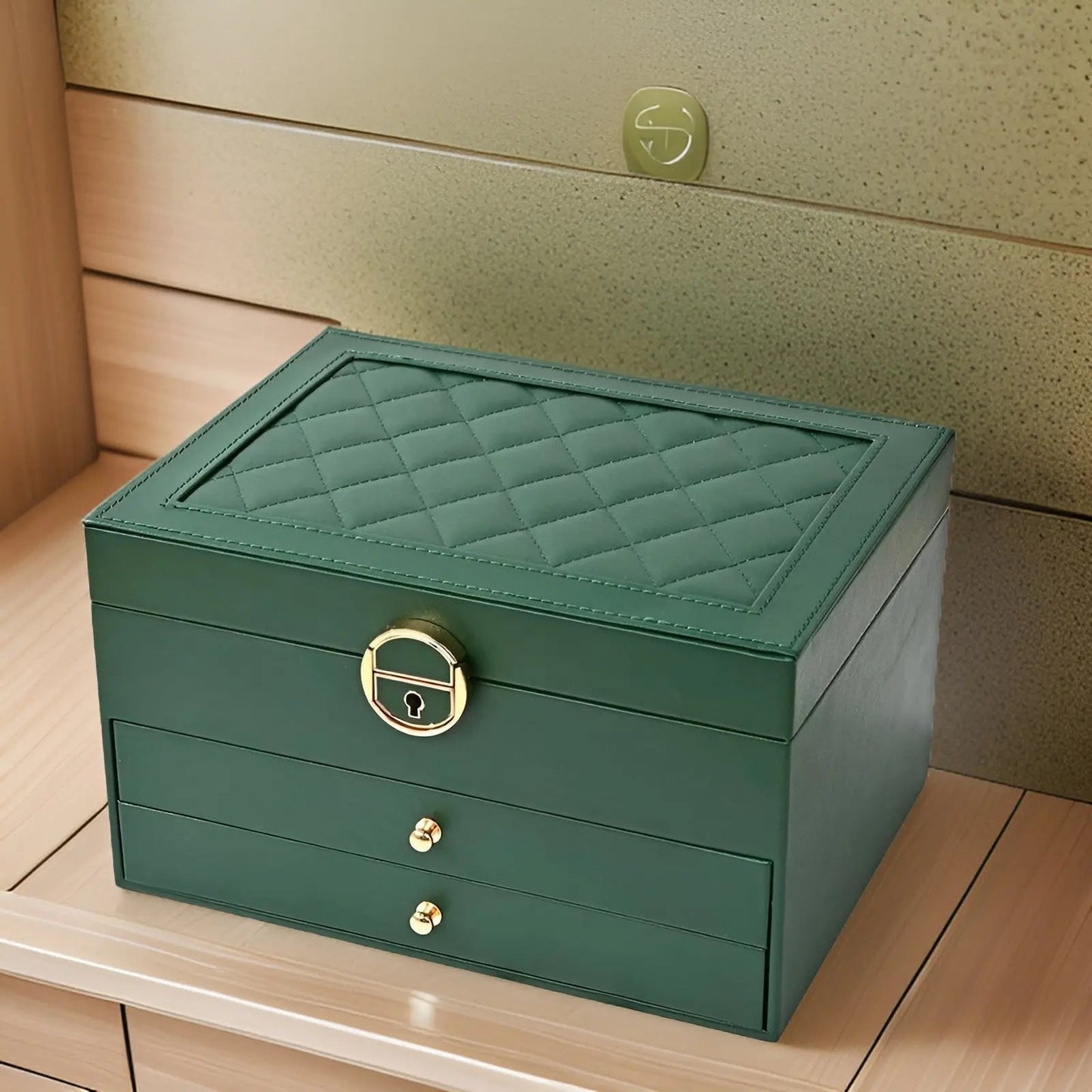 Grüne Schmuckschatulle aus Leder mit Rautenmuster und goldenen Griffen auf Holzregal.