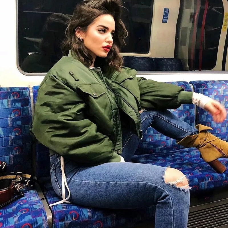 Frau in grüner Bomberjacke und zerrissenen Jeans auf U-Bahn-Sitz, modischer urbaner Stil.