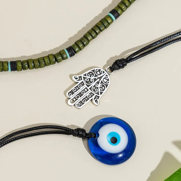 Halskette mit grünen Perlen, silbernem Hamsa-Anhänger und blauem Nazar-Amulett auf beigem Hintergrund.