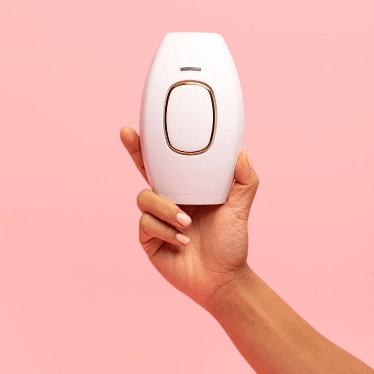 Hand hält weißes IPL-Haarentfernungsgerät vor rosa Hintergrund.