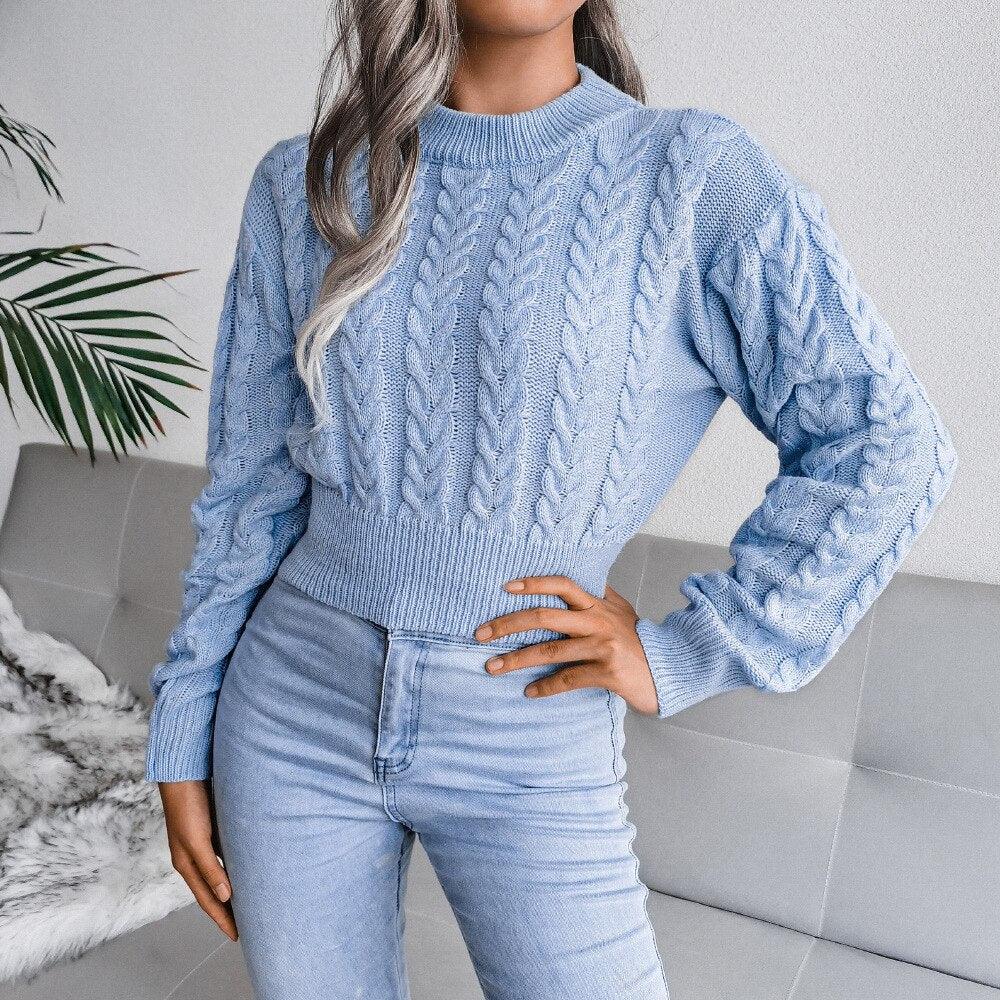 Frau in hellblauem Zopfmuster-Pullover und Jeans auf grauem Sofa, modisch, gemütlich.