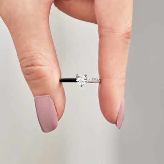 Hand hält silbernen Verlobungsring mit Herz-Diamant, elegantes Schmuckdesign, Nahaufnahme.