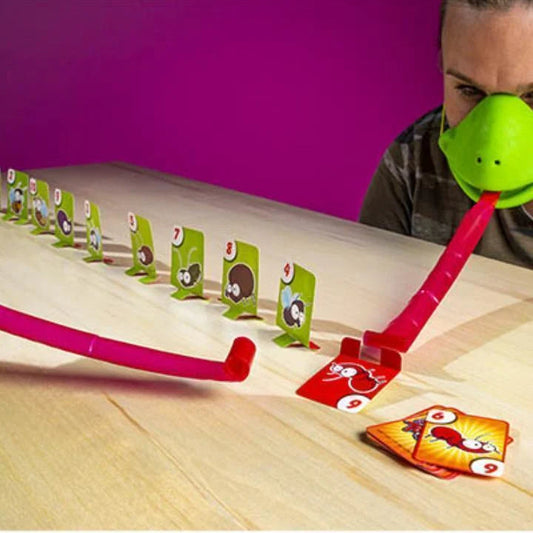 Person mit grünem Nasenaufsatz spielt lustiges Kartenspiel auf Holztisch, bunte Karten.