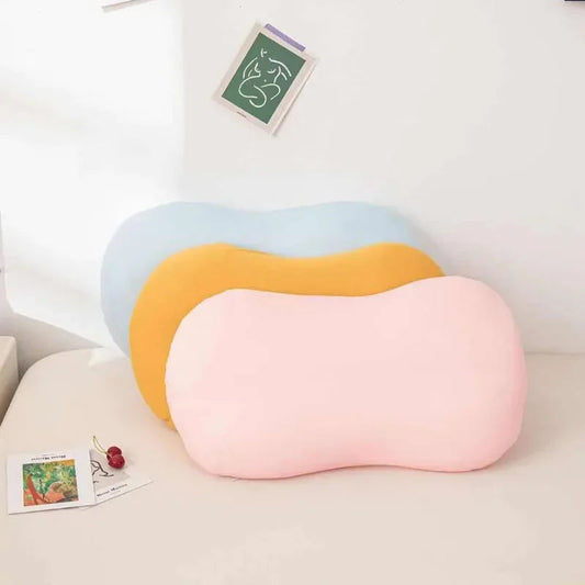 Drei ergonomische Kissen in Rosa, Gelb und Blau auf einem Bett, ideal für Nackenunterstützung.