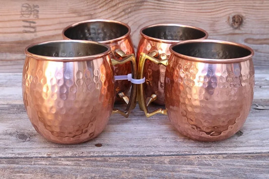 Vier gehämmerte Kupferbecher mit Griffen auf Holztisch, ideal für Moscow Mule Cocktails.
