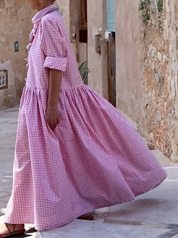 Frau in rosa kariertem Sommerkleid, knöchellang, auf gepflasterter Straße spazierend.