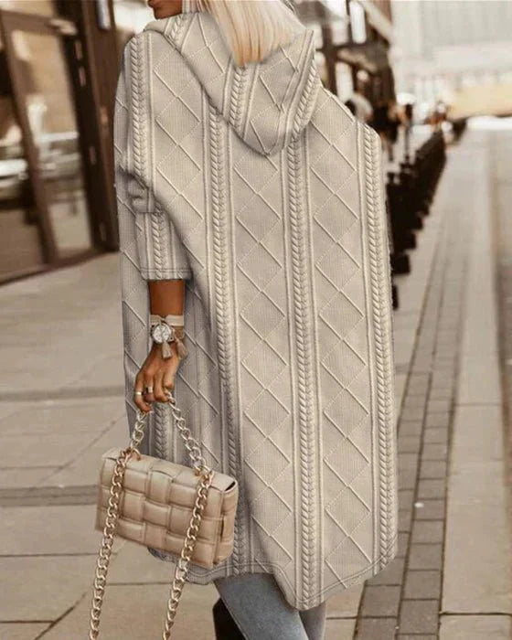 Frau in langem, grauem Strick-Cardigan mit Kapuze, hält beige gesteppte Handtasche.