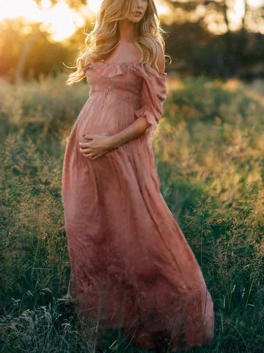 Schwangere Frau im rosa Maxikleid in einem Feld bei Sonnenuntergang, romantische Schwangerschaftsfotografie.