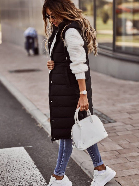 Frau in schwarzer, knielanger Steppweste, weiße Tasche, Jeans, Sneakers, Herbstmode.