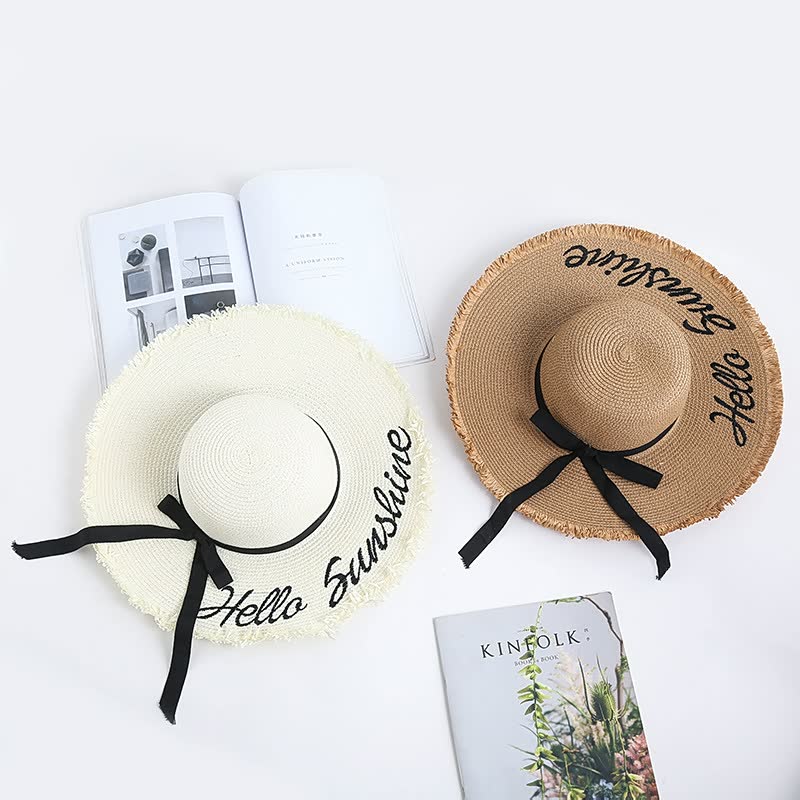 Zwei Strohhüte mit Schriftzug "Hello Sunshine", einer in Weiß, einer in Braun, auf weißem Hintergrund.