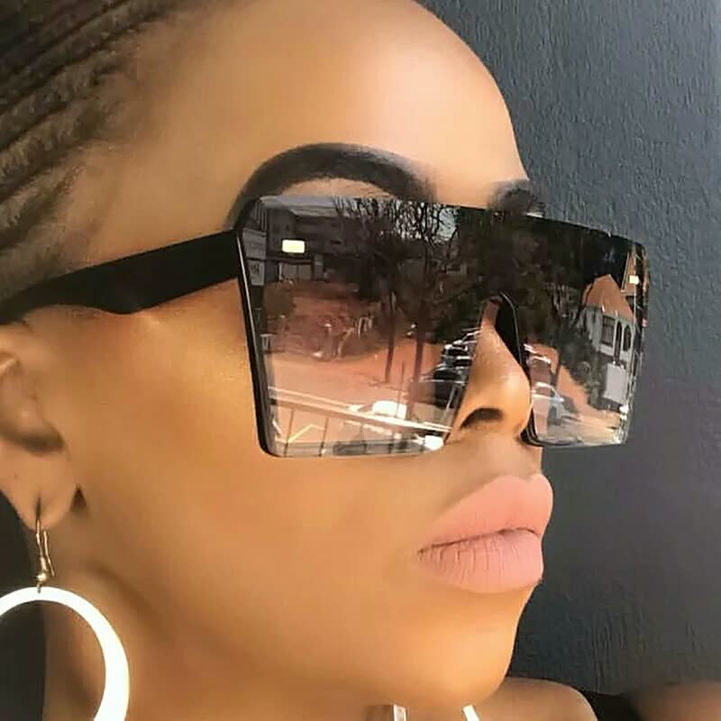 Frau mit übergroßer, eckiger Sonnenbrille, schwarzer Rahmen, verspiegelte Gläser, modisch.