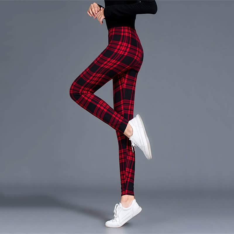 Frau in rot-schwarz karierten Leggings, schwarze Oberteil, weiße Sneaker, grauer Hintergrund.