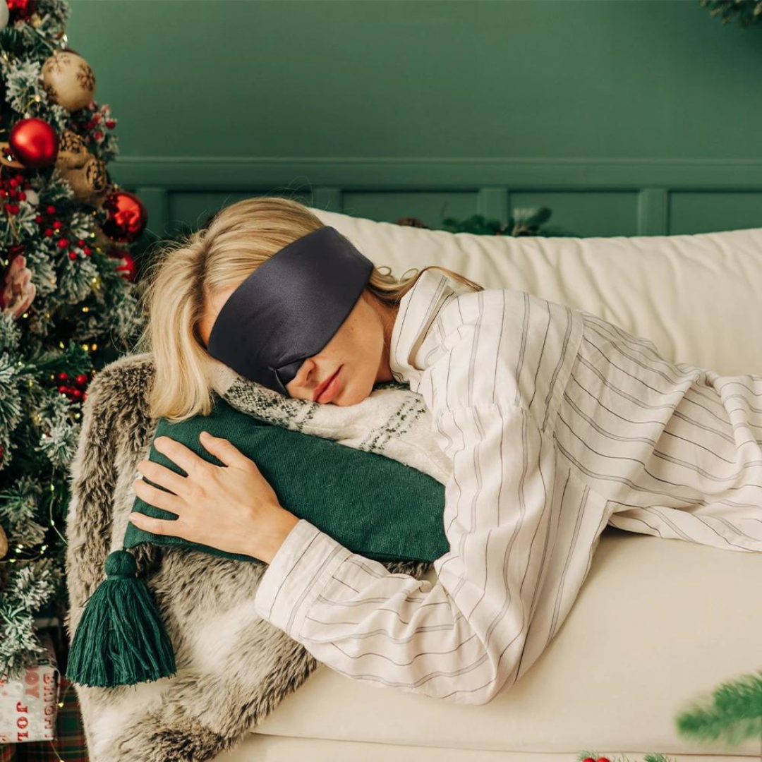 Frau mit schwarzer Schlafmaske auf Sofa, Weihnachtsdeko, Pyjama, Kissen, Entspannung.