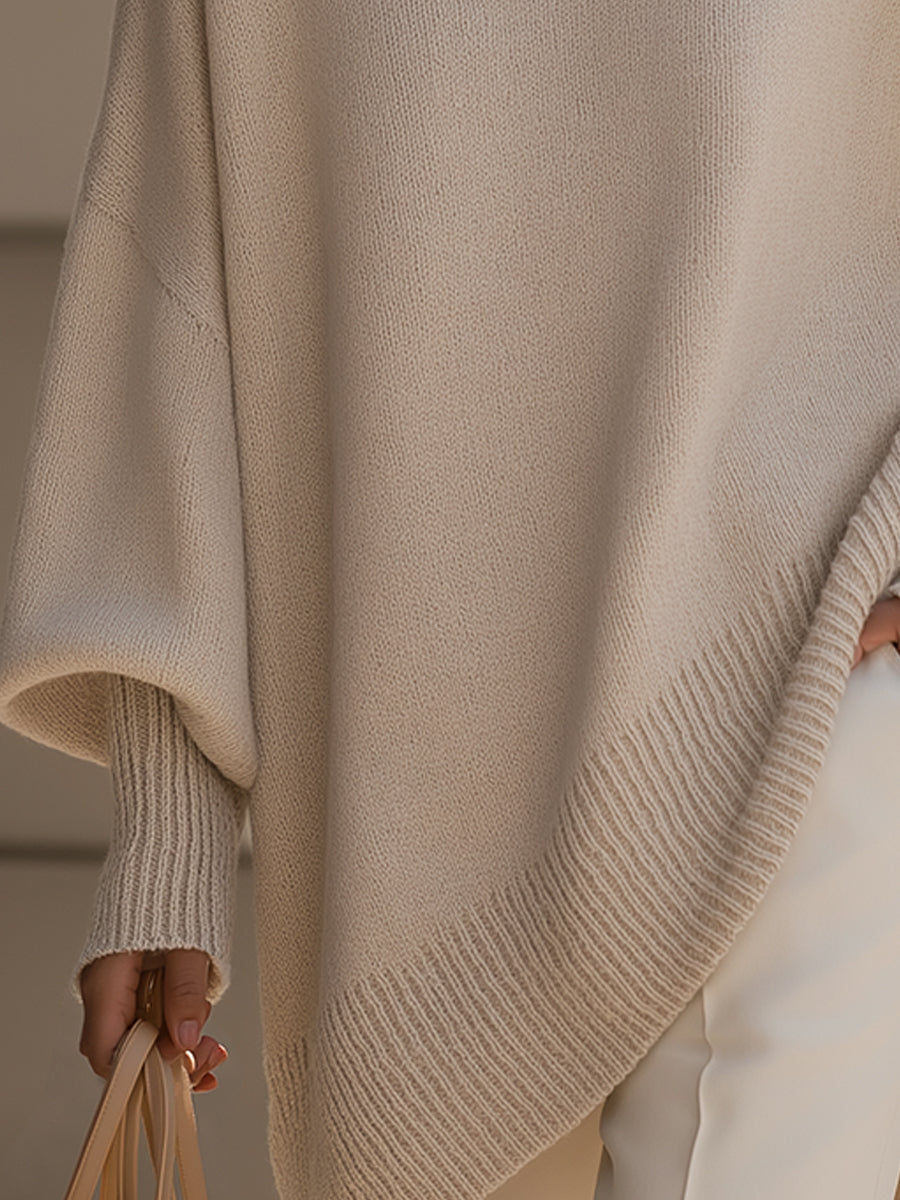 Detalj av ribbad nederkant och muddar på beige poncho, handen håller en väska 4