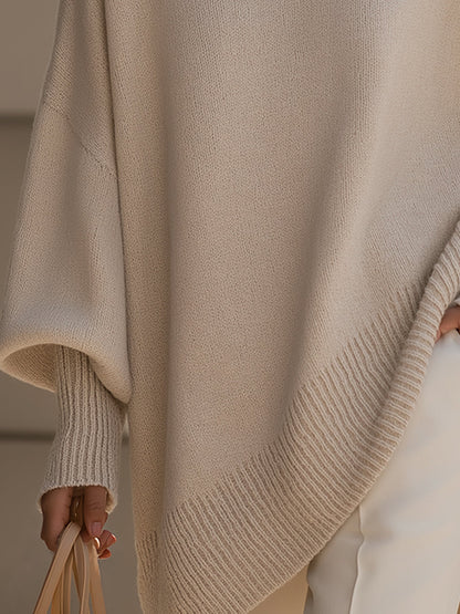 Detalj av ribbad nederkant och muddar på beige poncho, handen håller en väska 4