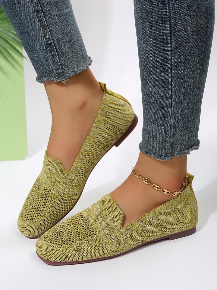 Gulgröna stickade slip-on-skor på en modell i grå jeans med kedja runt vristen, sedda från sidan mot ljus bakgrund. 18