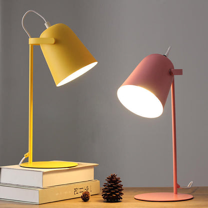 Två tända bordslampor, en gul och en rosa, på en träskiva med böcker och en kotte. 5