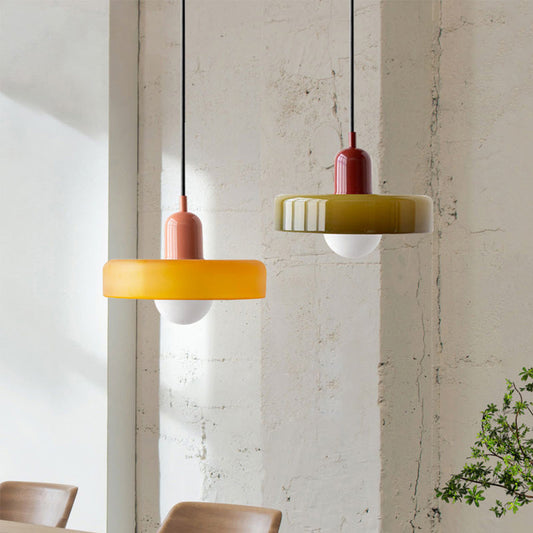Zwei moderne Hängelampen aus Glas in Gelb und Grün vor Betonwand.
