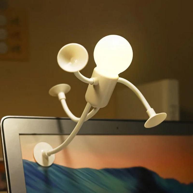 Vit tänd lampfigur klättrar upp på kanten av en laptopskärm med sugproppar på händer och fötter. 7