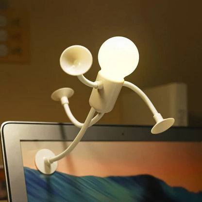 Vit tänd lampfigur klättrar upp på kanten av en laptopskärm med sugproppar på händer och fötter. 7