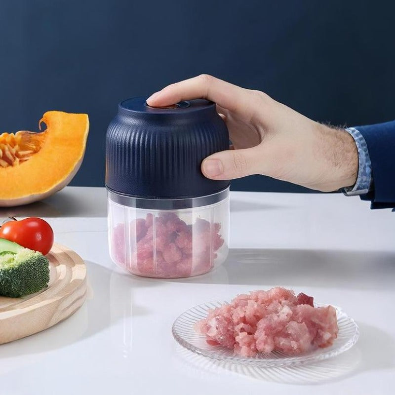 Hand trycker på mörkblå mini-matberedare fylld med rosa köttfärs, bredvid en tallrik med färs, pumpa, broccoli och tomat. 1