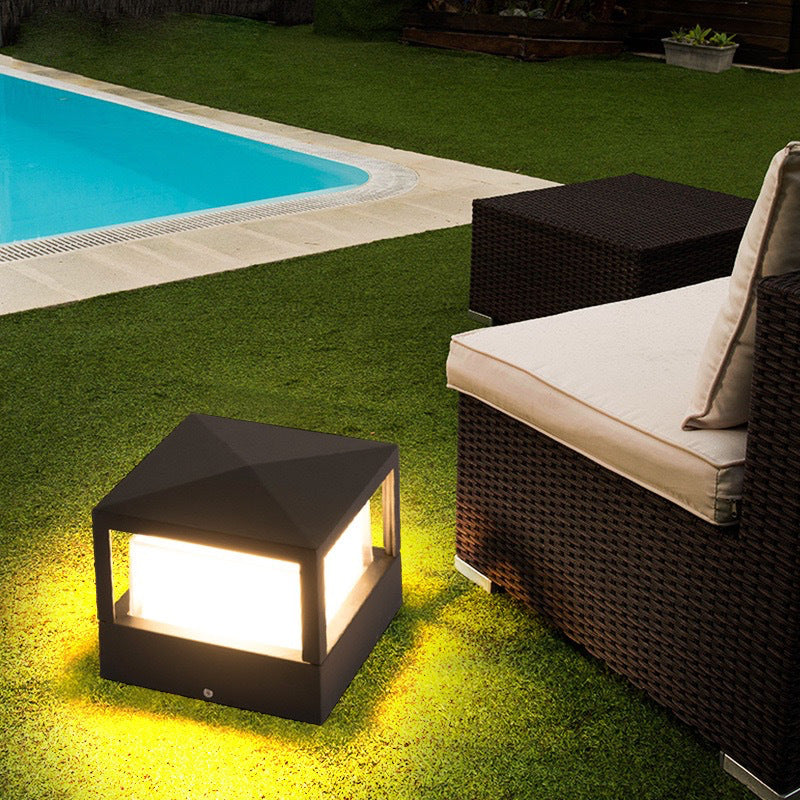 Svart fyrkantig lampa med pyramidformat tak står på gräset och lyser nära en pool och en rottingsoffa. 4
