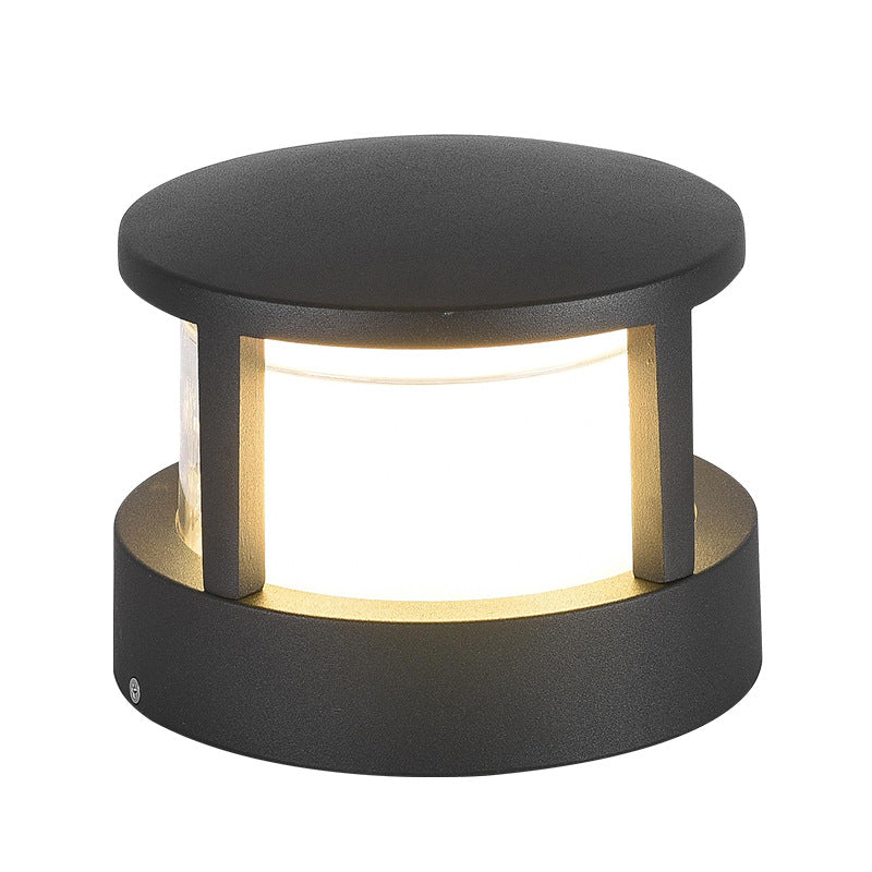 Rund svart lampa med platt tak sedd nära framifrån, varm vit skärm lyser mellan tre stolpar. 12