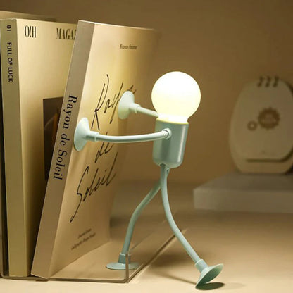 Ljusgrön tänd lampfigur trycker mot en bok med båda händerna som om den håller upp bokstödet på en hylla. 9