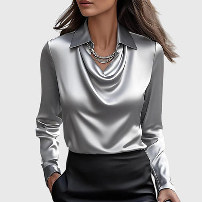 Modell bär blusen i glansigt silvergrått satin med draperad hals och krage, tillsammans med svart kjol och halsband. 2