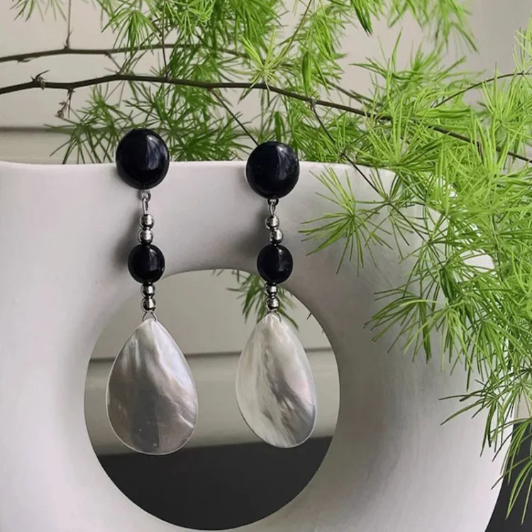 Schwarze und perlmuttfarbene Ohrringe, Tropfenform, vor grünem Farn, eleganter Schmuck.