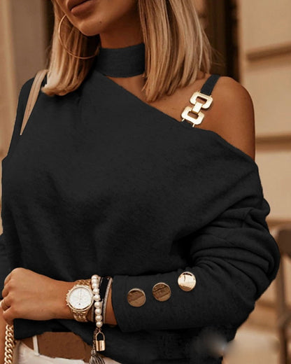 Frau in schwarzem, schulterfreiem Pullover mit goldenen Knöpfen und Schmuck.