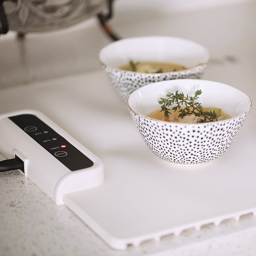 Zwei Schalen mit Suppe auf weißem Tisch, dekoriert mit Thymian, neben digitalem Heizgerät.