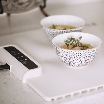 Zwei Schalen mit Suppe auf weißem Tisch, dekoriert mit Thymian, neben digitalem Heizgerät.