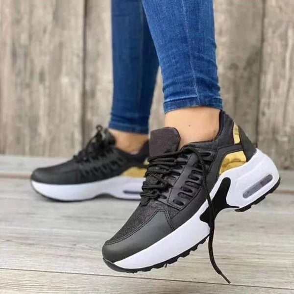 Schwarze Damen-Sneaker mit goldenen Akzenten, weiße Sohle, Freizeitschuhe, Holz-Hintergrund.